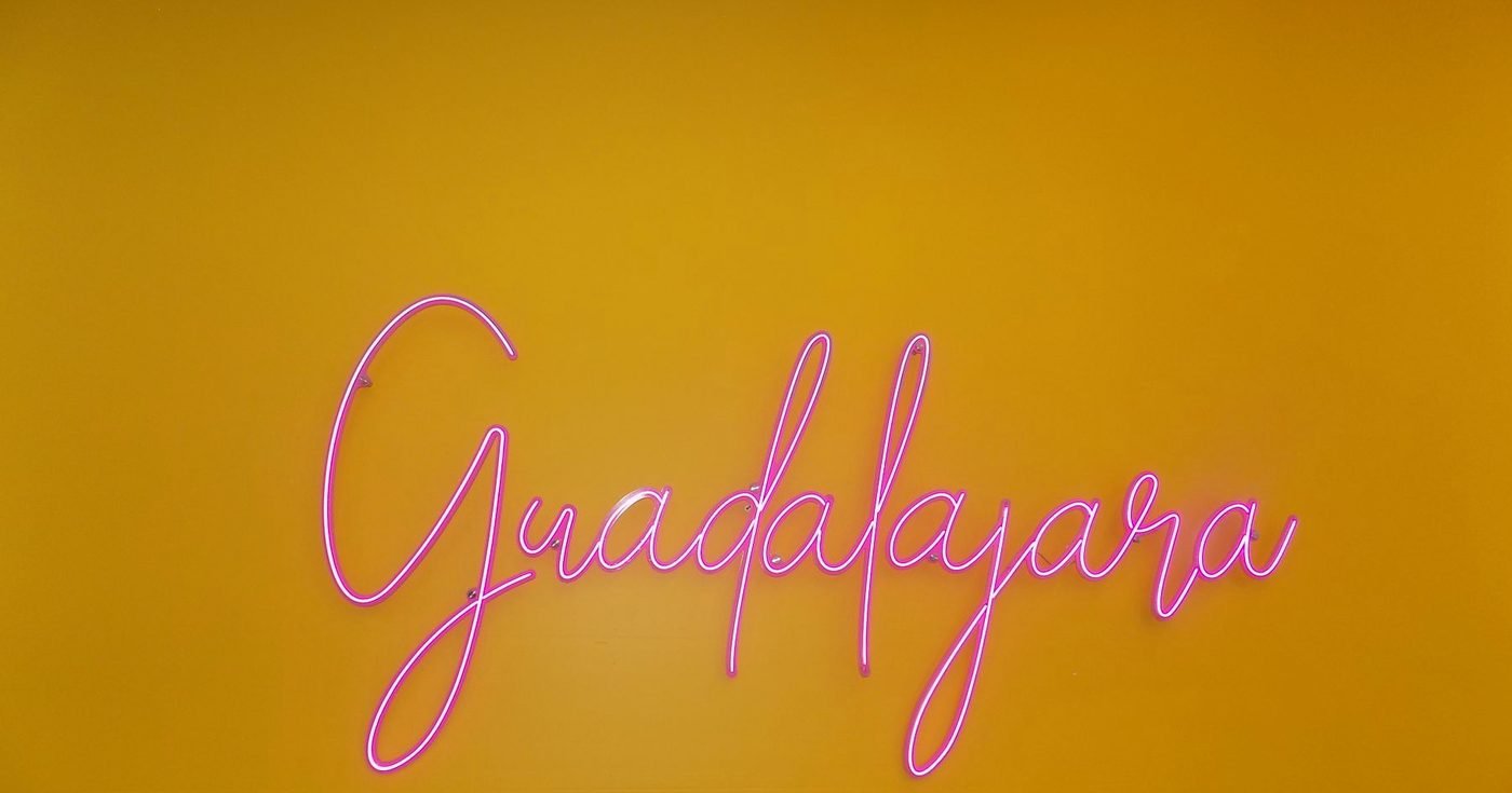 Letrero de neón rosa con letra cursiva sobre una pared amarilla