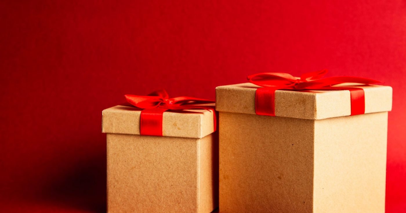 Dos cajas de cartón kraft con lazo rojo sobre una superficie roja